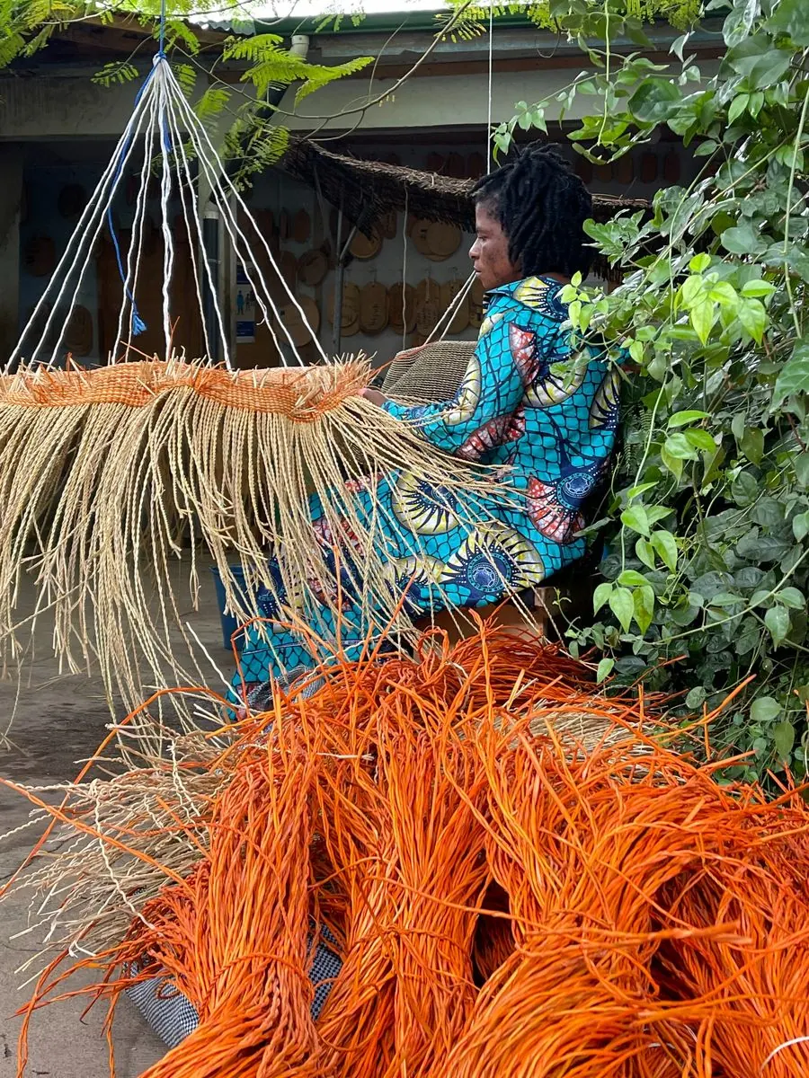 A basket maker weaving an orange basket suspended upside down