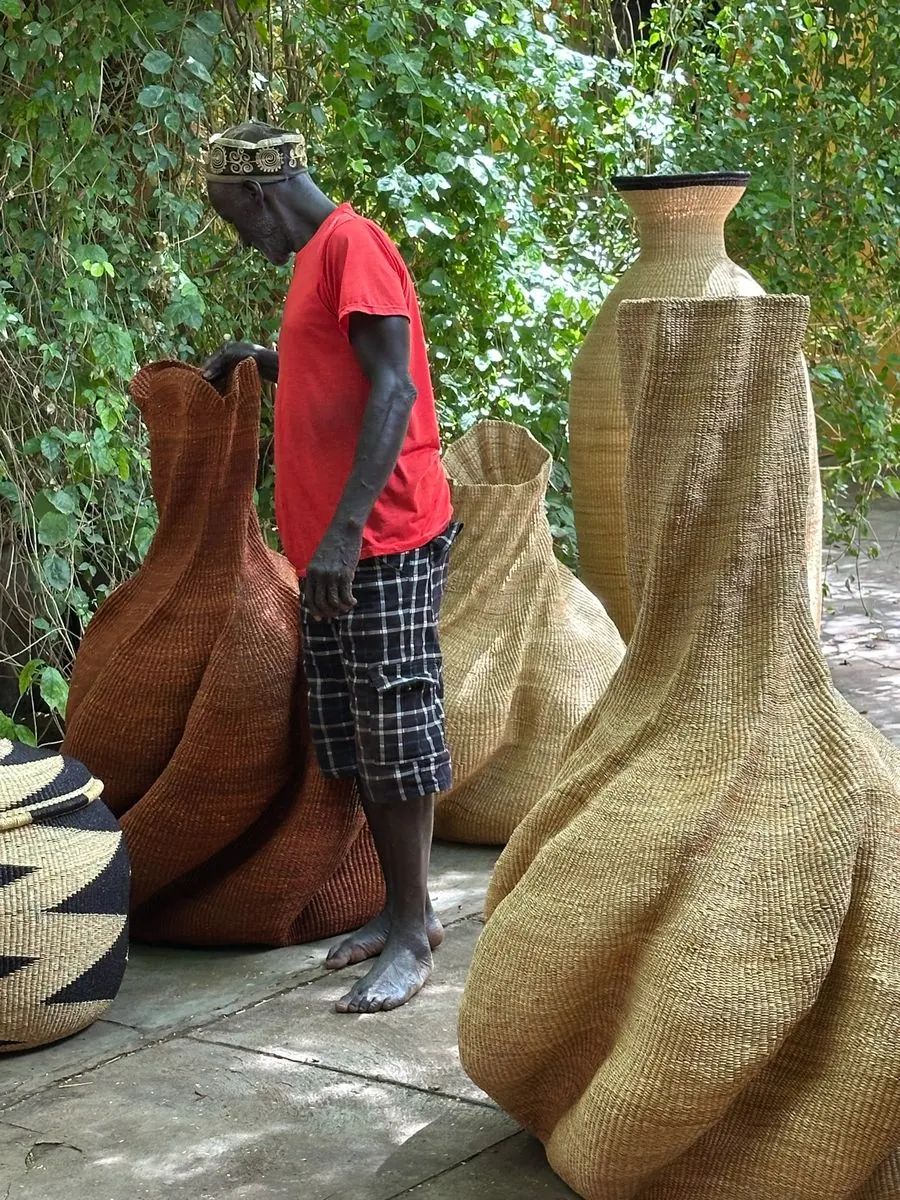 A basket maker standing beside two large sculptural woven baskets