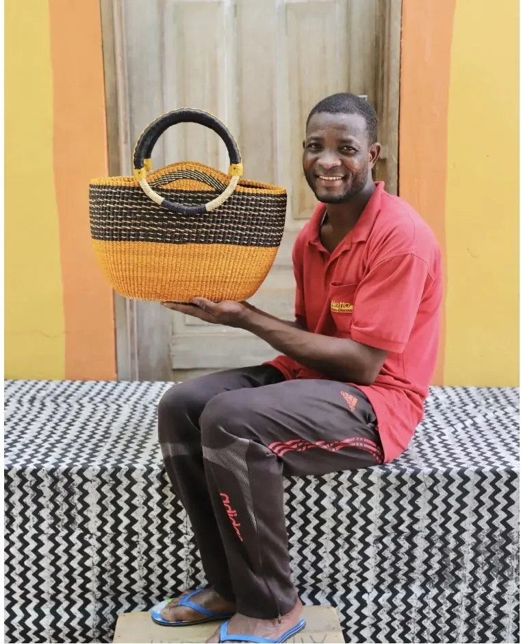 A basket maker seated with a finished round market basket